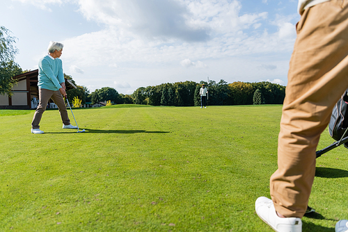 senior asian man playing golf with wealthy interracial friends on lawn