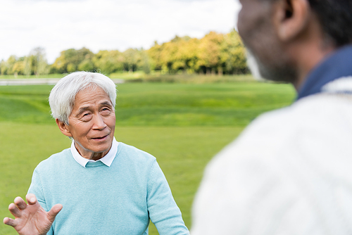 senior asian man looking at blurred african american friend