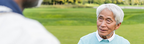 senior asian man looking at blurred african american friend, banner