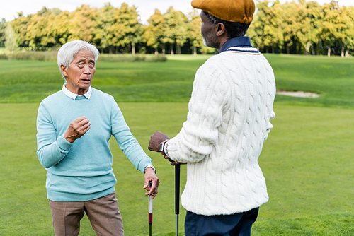 senior asian man talking with african american friend in flat cap