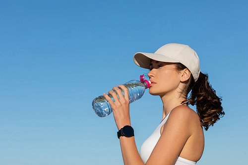 fit young woman in  drinking refreshing water against blue sky