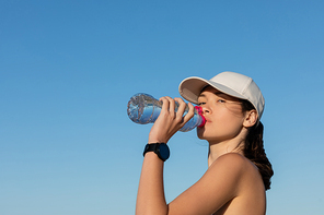 sportive woman in  drinking refreshing water against blue sky
