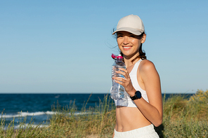 happy and sportive woman in  holding bottle with water near ocean