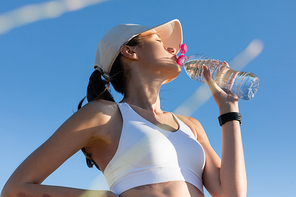 low angle view of sportive woman in  and sports bra drinking water against blue sky