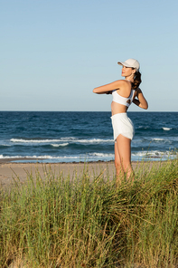 young fit woman in shorts and sports bra exercising near blue sea on beach