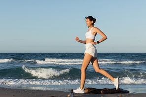 full length of happy young sportive woman jogging near sea in summer