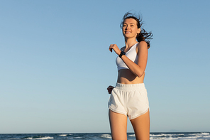 low angle view of happy young sportive woman jogging near sea in summer
