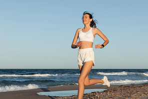 smiling young woman in sportswear jogging near sea in summer