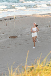 young sportive woman in  and wireless earphone running on sand near sea