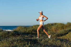 sportive woman in  and wireless earphone running on grass near sea