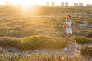 young sportive woman in wireless earphone running during sunset