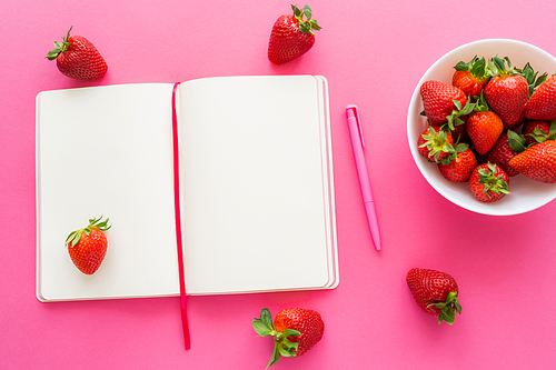Top view of natural strawberries near open notebook on pink background