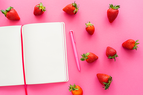 Top view of organic strawberries and open notebook on pink background