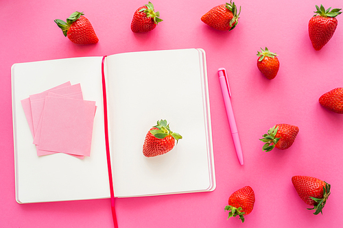 Top view of notebook and sticky notes near fresh strawberries on pink background