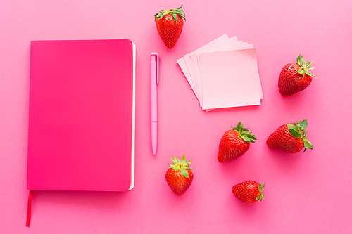 Top view of sticky notes near ripe strawberries and notebook on pink background