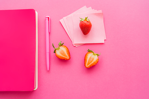 Top view of organic strawberries near sticky notes and notebook on pink background
