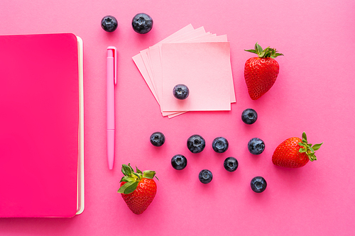 Top view of berries near sticky notes and notebook on pink surface