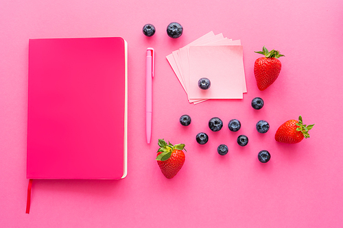 Top view of fresh berries near sticky notes and notebook on pink surface