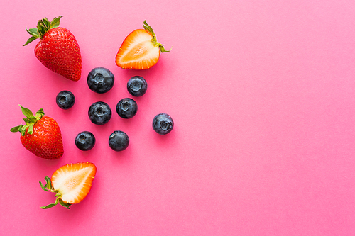 Top view of natural blueberries and strawberries on pink background