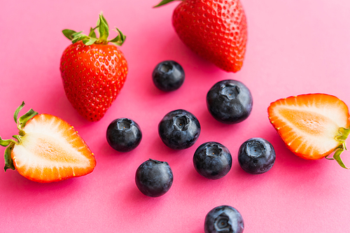 Close up view of sweet strawberries and blueberries on pink background
