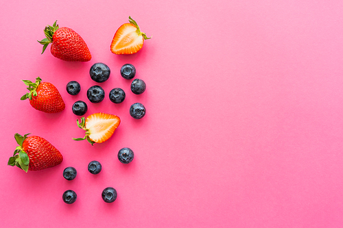 Top view of fresh blueberries and sweet strawberries on pink background