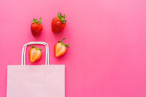 Top view of fresh strawberries near shopping bag on pink background