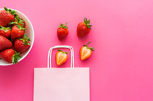 Top view of ripe strawberries and shopping bag on pink background