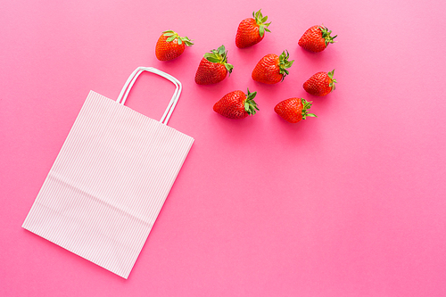 Top view of shopping bag near organic strawberries on pink background