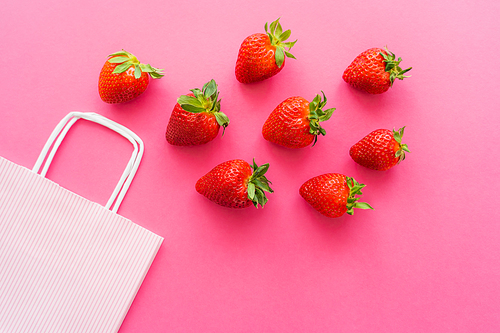 Top view of fresh strawberries with leaves near shopping bag on pink background