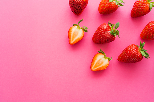 Top view of whole and cut strawberries on pink background