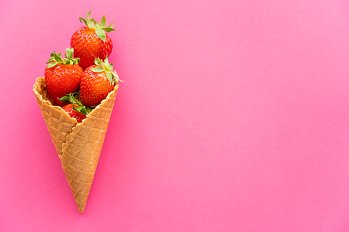 Top view of fresh strawberries in waffle cone on pink background