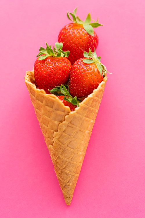 Top view of juicy strawberries in waffle cone on pink background