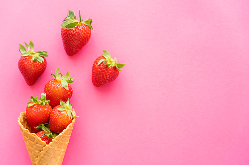 Top view of strawberries with leaves in waffle cone on pink background