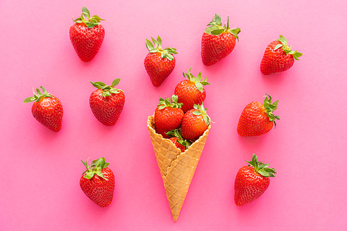 Top view of ripe strawberries and waffle cone on pink background