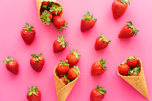 Top view of strawberries near waffle cones on pink background