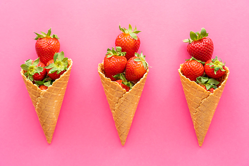 Flat lay with strawberries in waffle cones on pink background