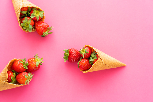 Flat lay of fresh strawberries in waffle cones on pink background