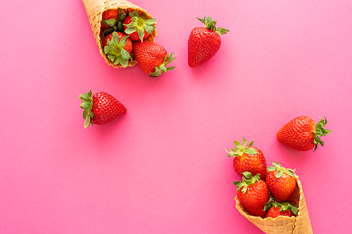 Top view of fresh strawberries with leaves in waffle cones on pink background