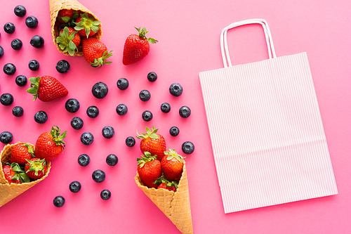 Flat lay with shopping bag near fresh berries and waffle cones on pink background