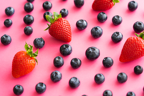 Close up view of juicy strawberries and blueberries on pink background