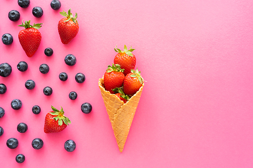 Flat lay with strawberries in waffle cone and blueberries on pink background