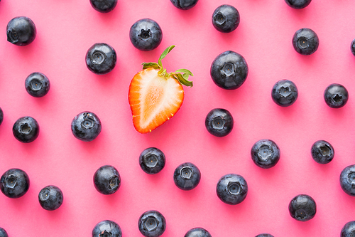 Flat lay of cut strawberry near blueberries on pink background