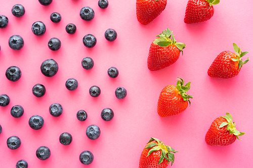 flat lay of juicy blueberries near strawberries on pink background