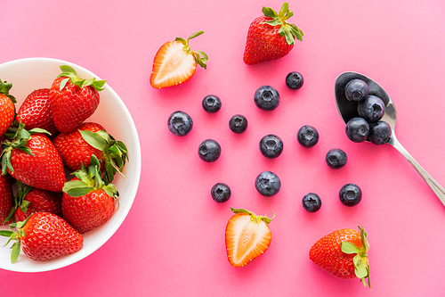 Flat lay with strawberries and blueberries near bowl and spoon on pink background