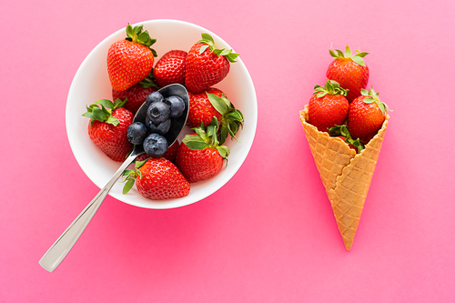 Top view of berries in bowl and waffle cone on pink background