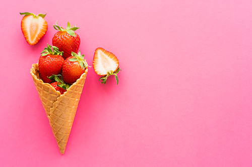 Top view of sweet waffle cone and strawberries on pink background