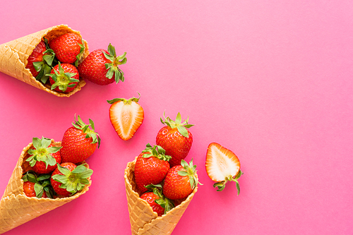 Top view of sweet strawberries with leaves in waffle cones on pink background