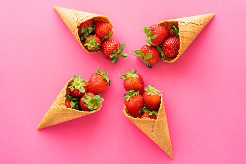 Flat lay with organic strawberries in sweet waffle cones on pink background