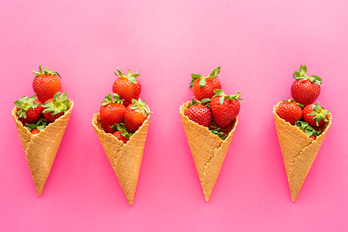 Flat lay with ripe berries with leaves in waffle cones on pink background