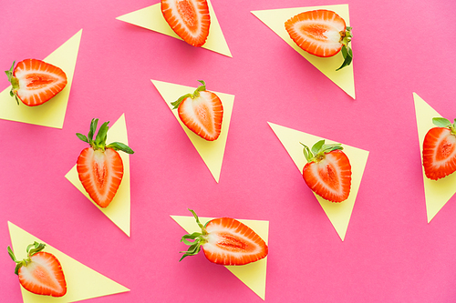 Flat lay with cut strawberries on yellow triangles on pink background